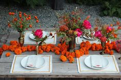 the table is set with orange and pink flowers in vases, napkins, and silverware