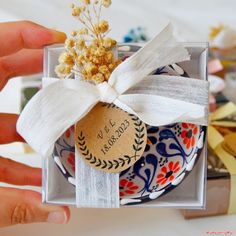 a person holding a small plate in a box with a ribbon around it and some flowers on top