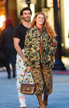 a man and woman walking down the street in camouflage clothing, one carrying a brown bag