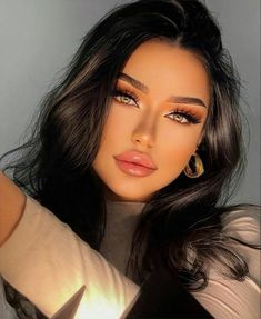 a woman with long black hair wearing gold hoop earrings and brown eyeshadow, posing for the camera