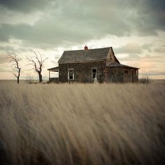 an old house sits in the middle of a field with tall grass and bare trees