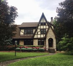 a house with flowers in the front yard and trees on either side, near a sidewalk