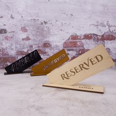 three wooden signs sitting next to each other on top of a white surface with brick wall in the background