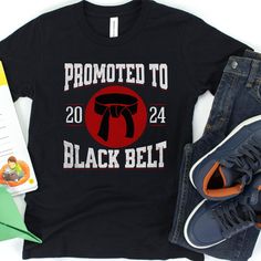 Celebrate a milestone in your young martial artist's journey with this personalized "Promoted to Black Belt" t-shirt! 🥋 This custom tee is not only a symbol of hard-earned success but also a keepsake that commemorates their dedication and the year they achieved this impressive rank. Crafted from comfortable materials that stand up to rigorous training sessions or casual wear, this tee is perfect for any occasion. -Personalize with the year of achievement -Durable and comfortable fabric for acti Black Team Spirit T-shirt With Letter Print, Black School Spirit T-shirt For Sports Events, Black Graphic Tee With Team Name, Sporty Black T-shirt With Custom Print, Black School Spirit T-shirt With Screen Print, Black T-shirt With Custom Print For Fans, Black Custom Print Fan Apparel T-shirt, Black Custom Print T-shirt, Fan Apparel, Black Custom Print Fan T-shirt