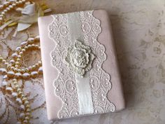 a pink and white book sitting on top of a lace covered tablecloth next to pearls