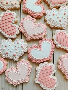 decorated cookies with pink and white icing are arranged on a wooden surface, including hearts