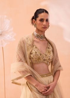 An elegant set features a V-neck blouse embellished with intricate zardozi floral motifs, paired with a lehenga adorned with large floral motifs and a matching dupatta. The ensemble combines sophisticated detailing with timeless charm, making it a perfect choice for any special occasion. Festive V-neck Lehenga With Dupatta, Festive V-neck Sets With Resham Embroidery, Designer Bollywood Lehenga With V-neck, Bollywood Style V-neck Lehenga For Designer Wear, Bollywood Style Lehenga With V-neck Dupatta, Bollywood Style V-neck Lehenga With Dupatta, Traditional V-neck Palazzo Set For Wedding, Festive V-neck Choli With Mirror Work, Anarkali Palazzo Set With V-neck For Wedding