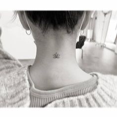 a woman's neck with a small lotus tattoo on the back of her neck