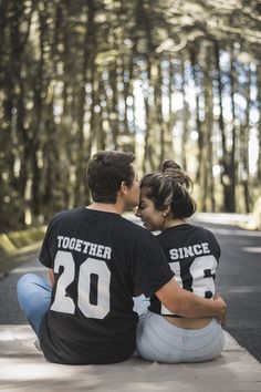 a man and woman sitting on the ground in front of trees with their backs to each other