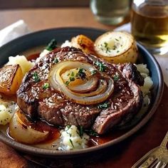 steak with onions, potatoes and gravy on a plate next to a glass of beer