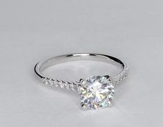 a white gold engagement ring with diamonds on the band and a round center stone in the middle