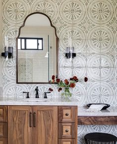 a bathroom with a sink, mirror and wooden cabinet in front of a wallpapered background