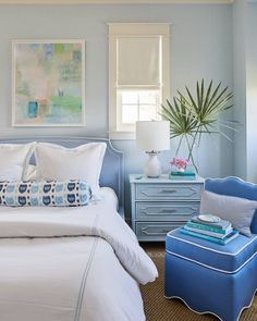 a bedroom with blue and white furniture and paintings on the wall, along with an ottoman