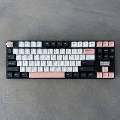 a black and white keyboard with pink keys on the bottom half, sitting on a gray surface