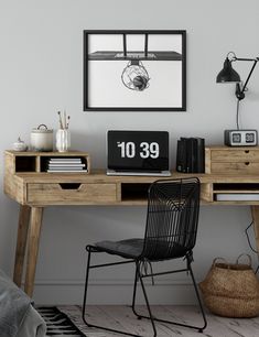 a wooden desk topped with a computer monitor next to a black chair and book shelf