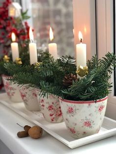 some candles are sitting on a window sill with pine cones and greenery in them