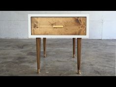 a white and wood table with two legs on concrete flooring next to a wall