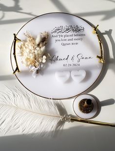 a white plate with a gold rim and some flowers on it next to a feather