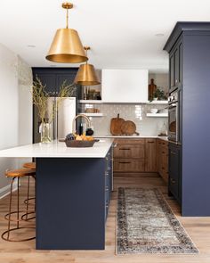 a kitchen with blue cabinets and white counter tops, gold pendant lights over the island