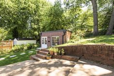 a small brick house sitting in the middle of a lush green yard with steps leading up to it