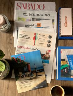 newspapers and magazines on a wooden table with a cup of coffee next to the newspaper