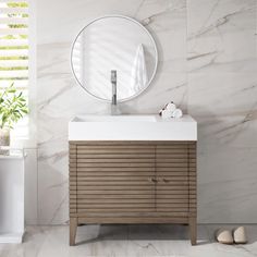 a white sink sitting under a round mirror on top of a wooden cabinet next to a wall