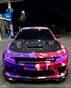 a camo colored car is parked in front of a gas station at night with its hood up