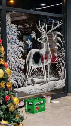 a decorated christmas tree in front of a window with a deer and snow scene on it