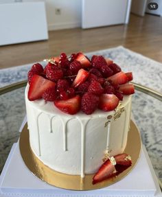 a cake with white frosting and strawberries on top sitting on a glass table