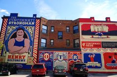 several large murals on the side of buildings in an urban area with cars parked nearby