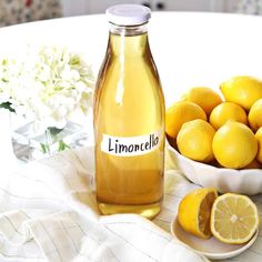 a bowl of lemons and a bottle of limoo on a table with flowers in the background