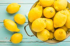 a bucket full of lemons sitting on top of a blue wooden table next to some cut in half lemons