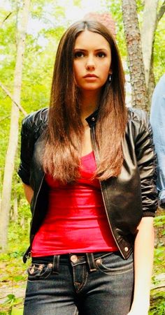 a woman standing in the woods with her hand on her hip and wearing a leather jacket