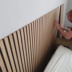 a man sitting on top of a bed next to a wooden headboard with vertical slats