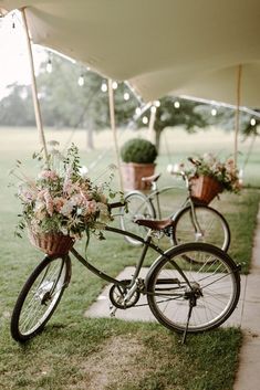 two bicycles with baskets full of flowers are parked under an awning on the grass