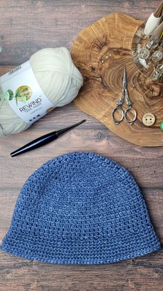 a crocheted blue hat sits on a wooden table next to scissors and yarn