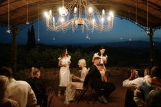 a group of people sitting around a table under a chandelier with lights hanging from it