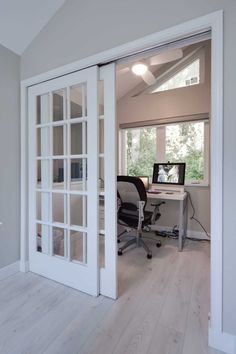 an open door leading to a computer desk in the middle of a room with white walls and wood floors