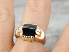 Designed in the Mid Century for a man, this vintage ring will be a striking statement piece on a lady. Lots of geometric lines are in play here, a wonderful contrast of straight lines and curves, including the domed, barrel cut onyx at the center. Most unusual, this stone has a grey stripe of a lighter colored agate along the outer edge! Metal: 10K Yellow Gold Main Stone: 1/2 Round Barrel Cut Onyx. 9mm Square Time Period: Mid Century Ring Size of Ring: 8 but can be sized to fit almost any finger (please see our sizing policies for more information). Retro Formal Rings With Polished Finish, Retro Rings With Polished Finish For Formal Occasions, Retro Polished Rings For Formal Events, Art Deco Rectangular Signet Ring With Polished Finish, Art Deco Black Enamel Rings For Formal Occasions, Formal Art Deco Rings With Black Enamel, Art Deco Onyx Ring With Black Enamel, Vintage Onyx Rings For Formal Occasions, Vintage Onyx Ring For Formal Events