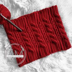 a red knitted scarf with a ball of yarn next to it and a crochet hook