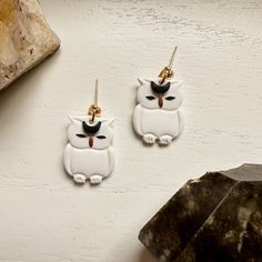 two white owl shaped earrings with gold earwires on top of a table next to a rock