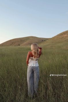 a woman standing in tall grass looking up at the sky