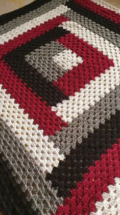 a crocheted blanket is laying on the floor with it's red, white and black colors