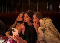 three women sitting at a table with one taking a selfie while the other holds her phone