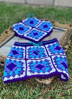 two blue and white crocheted squares sitting on top of green grass next to a mirror