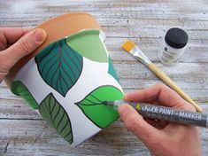 a person holding a cup with paint on it and some other items around it that are sitting on top of a wooden table