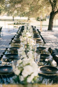 the long table is set with black plates and white flowers