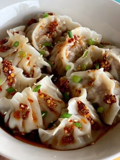 a white bowl filled with dumplings covered in sauce and topped with scallions