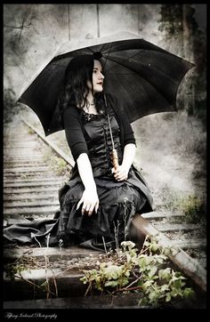 a woman sitting on the ground with an umbrella over her head and wearing a black dress