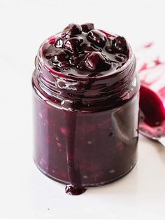 a jar filled with blueberry jam next to a spoon on top of a table